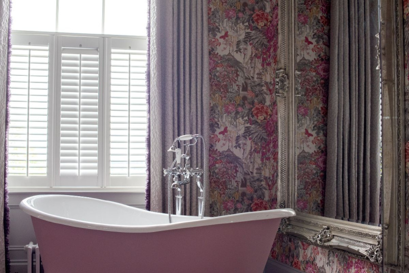 A pink roll top bath by the window with vibrant patterned wallpaper of purples and pinks at Rockhill House Estate Letterkenny donegal Hotel and spa